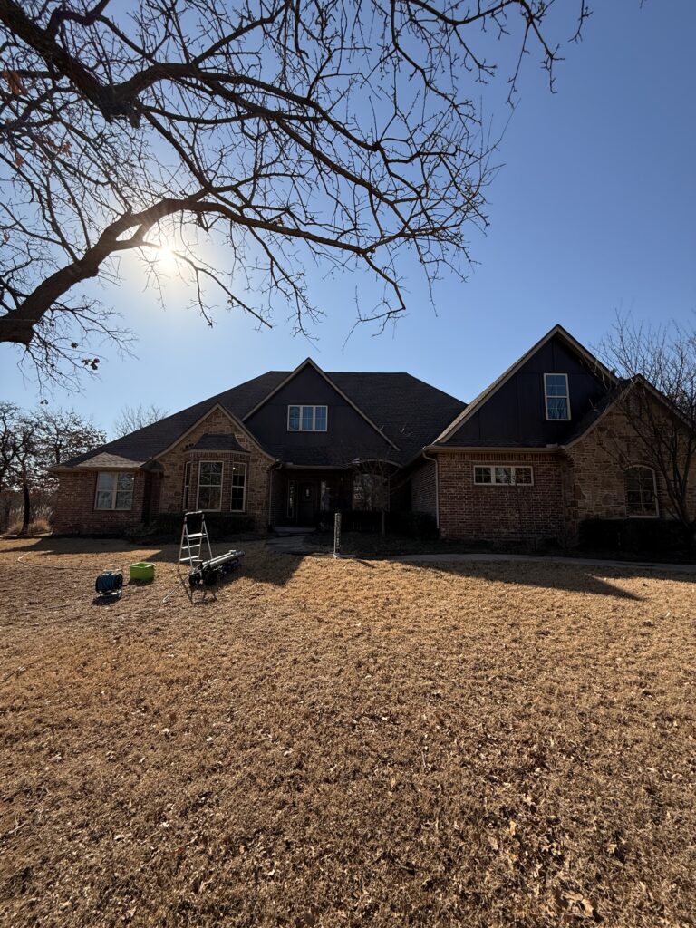 two-story house with bare trees and equipment on the ground indicating potential cleaning or maintenance work being done