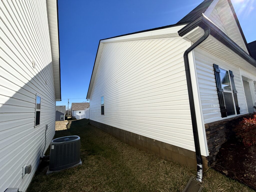 house washing a white vinyl siding with clear blue sky in background and well maintained lawn