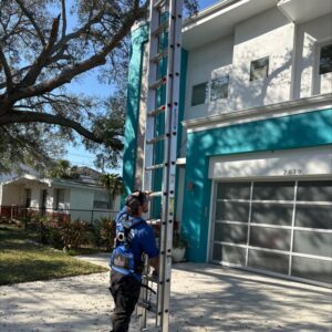 worker using a ladder to access the second story of a house for gutter or window cleaning services