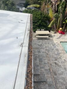 gutter cleaning with leaves and debris accumulated along the edge of a roof near outdoor seating and a pool area