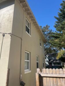 gutter cleaning and inspection on a light-colored house with windows and a wooden fence in a residential area