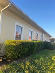 gutter cleaning service performed along the edge of a building with neatly trimmed hedges and clear blue sky