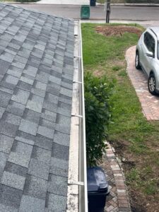 gutter cleaning service showing debris accumulation on the edge of a roof with a gray shingle surface and nearby vegetation