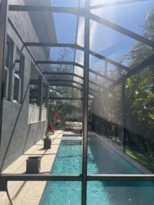 pool area with a screened enclosure and a clear blue pool surrounded by tropical plants and outdoor furniture