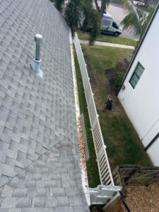 gutter cleaning service removing debris from a residential gutter with trees and a fence visible in the background
