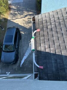 gutter cleaning services being set up with ladder and equipment on a residential roof near a parked vehicle