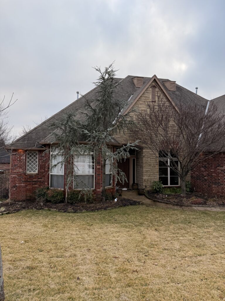 a residential home with a combination of brick and stone exterior landscaping includes grass and trees front entrance visible