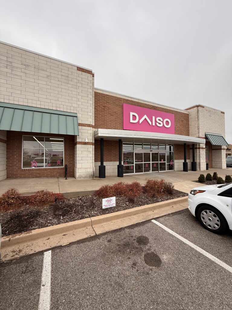 daiso retail store with large pink signage and clean exterior landscaping parking lot with a white vehicle nearby