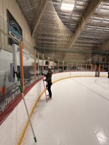 cleaning glass at an ice rink using long poles and specialized equipment
