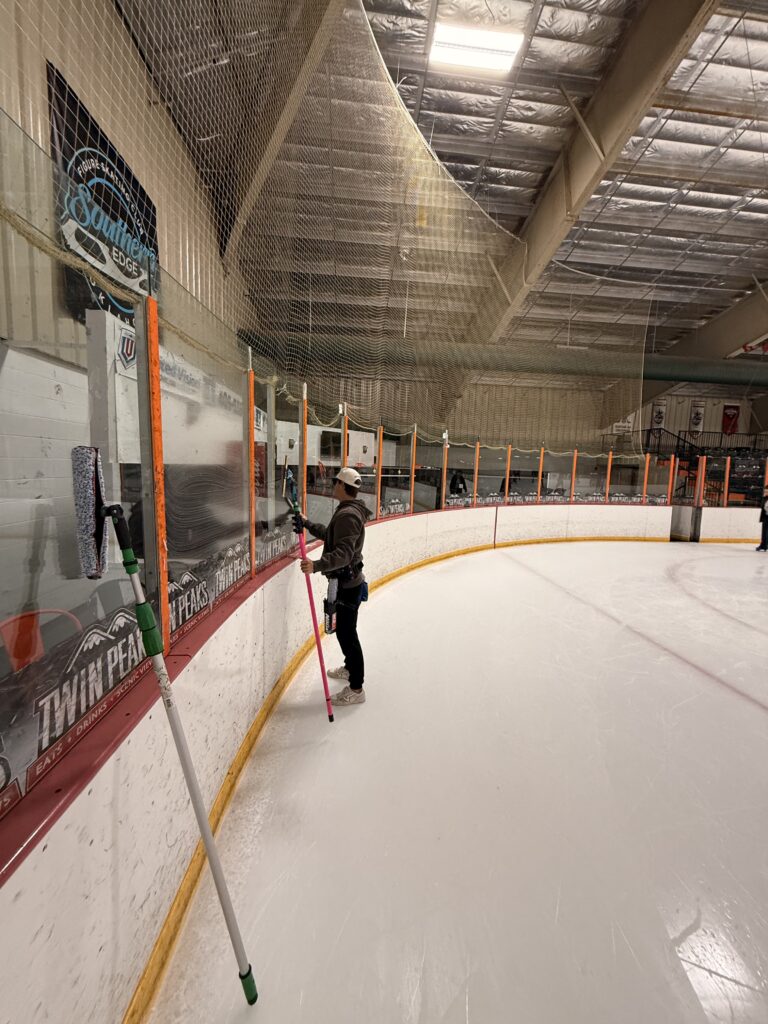 cleaning glass at an ice rink using long poles and specialized equipment