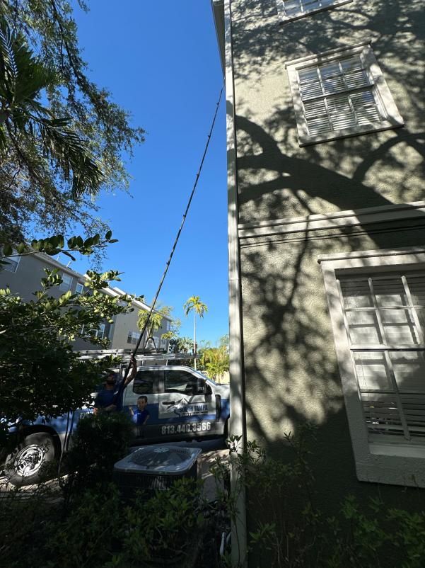 gutter cleaning service being performed on a tall building using a long pole and working from ground level