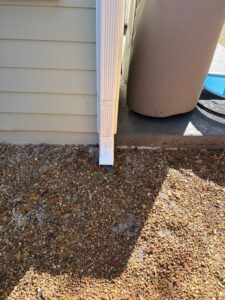 gutter downspout at the corner of a house with gravel landscaping and a storage container nearby