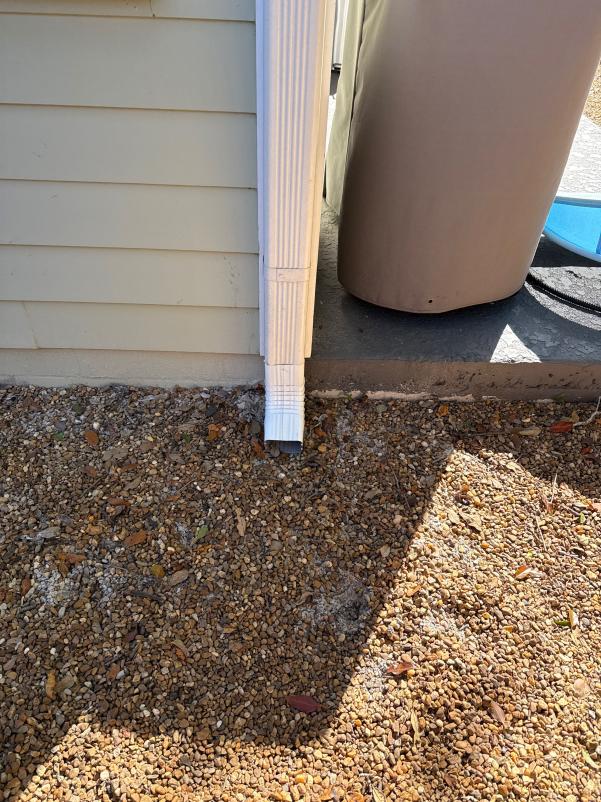 gutter downspout at the corner of a house with gravel landscaping and a storage container nearby