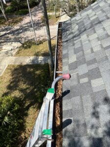 cleaning gutters with leaves and debris accumulation visible ladder positioned along the roof edge for accessibility