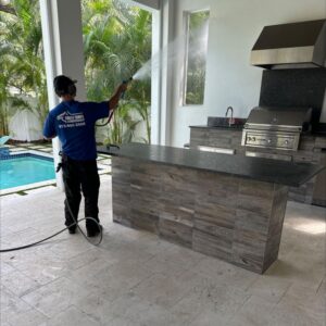 man using a pressure washer to clean an outdoor kitchen area beside a pool surrounded by tropical plants