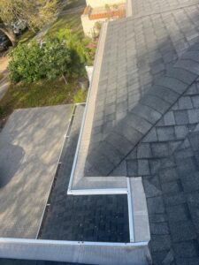 cleaning roof gutters with visible debris on shingles and a clear view of surrounding landscape and driveway