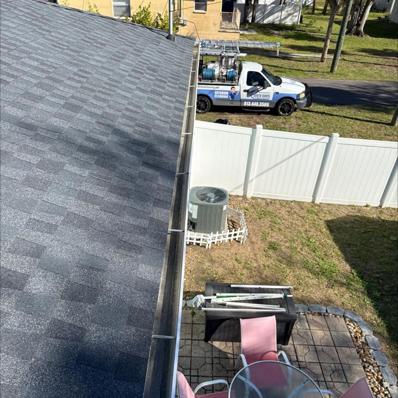 roof inspection with a focus on gutter cleaning and maintenance near residential area featuring a service truck in the background