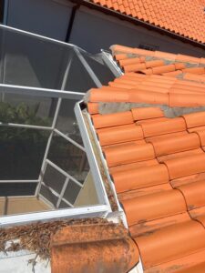 cleaning debris from roof tiles near a screened porch with buildup of leaves and dirt near the roof edge