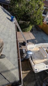gutter cleaning service with a ladder positioned on the roof near a boat in a driveway area