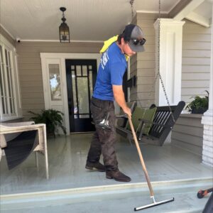 employee cleaning a porch floor using a long handled squeegee while wearing a blue shirt and protective eyewear