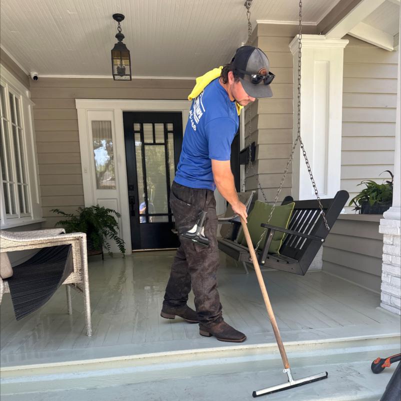 employee cleaning a porch floor using a long handled squeegee while wearing a blue shirt and protective eyewear