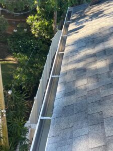 gutter cleaning service showing a gray shingle roof and a clean gutter system with lush greenery below