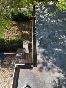 cleaning gutters with debris visible on the roof edge and leaves scattered in the yard below