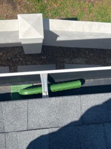 gutter cleaning tool resting in a gutter on a roof near green grass and concrete structures