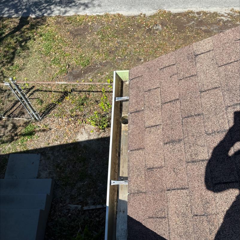 gutter installation on a sloped roof with visible flashing and nearby grass area in a residential setting