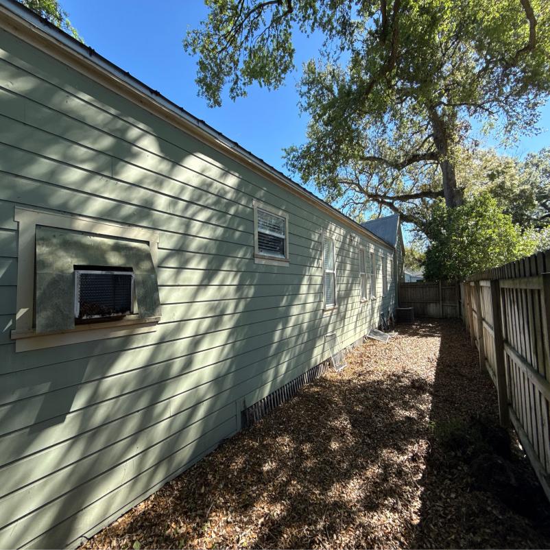 cleaning of green vinyl siding on a house with visible sunlight and surrounding trees and foliage