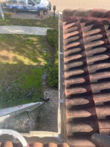 gutter cleaning service being performed using a ladder visible beside the house with a tile roof and landscaped yard