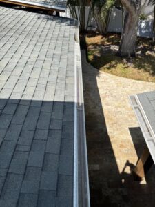 gutter cleaning services showing gutters installed along a sloped roof with shadows and a stone pathway visible below