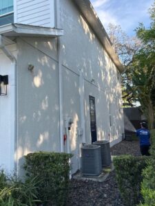 south tampa gutter and window cleaning performing a house wash on a light colored wall with landscaping and air conditioning units nearby