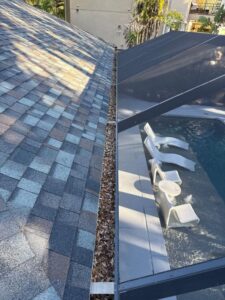 gutter cleaning service showing leaves and debris on a roof edge near a pool area with white lounge chairs