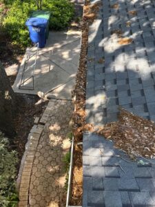 gutter cleaning with debris accumulation on the roof adjacent to a stone pathway and green trash bins in view