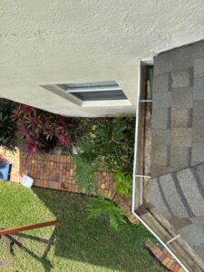 cleaning near a roof edge with a view of plants and a brick walkway in a residential area