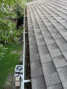 gutter cleaning service showing debris accumulation on edge of roof with surrounding greenery and air conditioning units visible