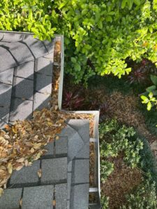 clogged gutters filled with leaves near a roof indicating a need for gutter cleaning services