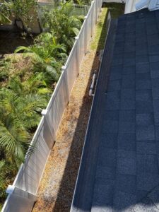 gutter cleaning along a residential property with gravel and landscaping visible beside a fence and roof edge