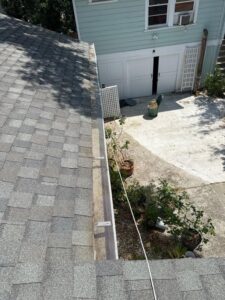 gutter cleaning service showing screened gutters on a sloped roof with plants and a patio area visible below