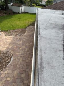 gutter installation with visible drainage system alongside a paved pathway and grassy area in a residential yard