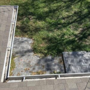 gutter cleaning with debris accumulation visible near paver stones and grass areas surrounding the gutters in need of maintenance