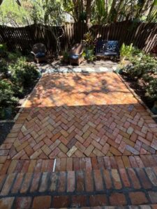brick patio cleaning with landscaping and seating areas visible in a shaded outdoor space surrounded by greenery