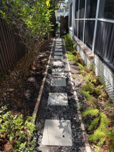 a narrow walkway with stone pavers bordered by gravel and plants on either side with wooden fencing in the background