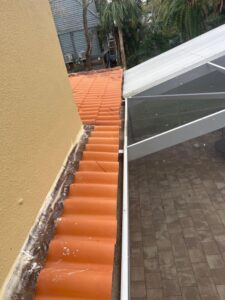 terracotta roof tiles with debris along the edge near a screened outdoor area and a beige wall in the background