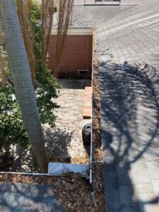 gutter cleaning service in progress with visible leaves and debris on roof near trees and brick patio area
