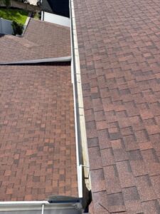 gutter installation on a brown shingle roof visible from an elevated angle with clear skies above
