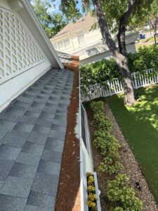 gutter cleaning showing debris removal from roof edge with a clear view of landscaping and well-maintained lawn areas