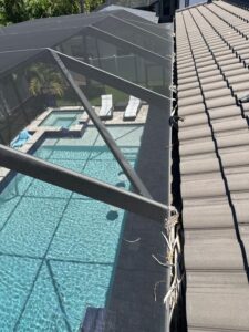 gutter cleaning service visible along the edge of a roof next to a screened pool area with clear water