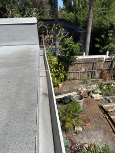 cleaning of a roof and gutter with visible trees and landscaping elements in the background